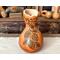 A handmade gourd vase with pinecones, branches and chickadees burned into the surface of the gourd. A wavy rim has been carved in the top.
